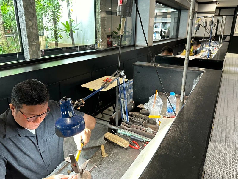 Master jeweler at a workbench with blue task lamps and precision tools